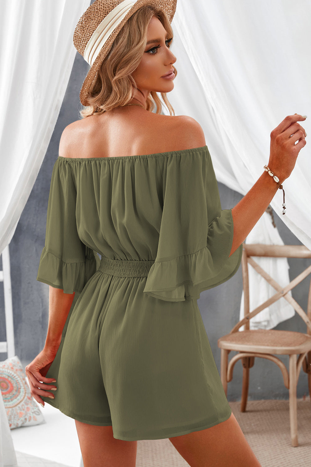 Back view of model wearing smocked waist romper with flounce sleeves.