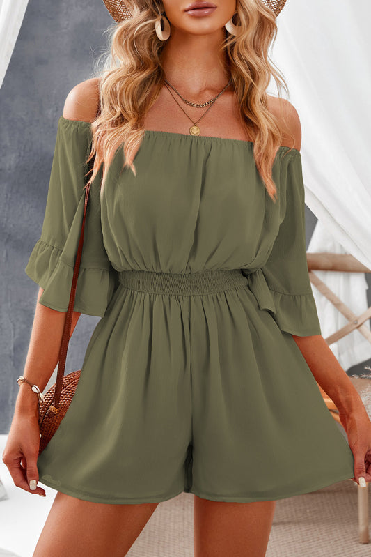 Front facing view of model wearing smocked waist romper. Style includes off shoulder flounce sleeves.